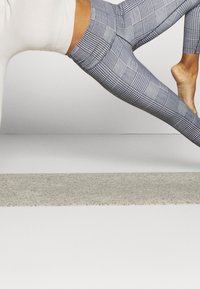 Legginsy w szarym wzórze z geometrycznym designem, wykonane z elastycznego materiału. Posiadają wysoki stan i gładką teksturę.