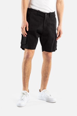 Bermudas negras de algodón, con bolsillos laterales y un corte relajado. Combinadas con zapatillas blancas, de largo hasta la rodilla.