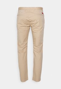 Pantalon slim beige pour homme vu de dos, avec passants de ceinture, deux poches passepoilées et une petite étiquette rouge sur la poche droite.
