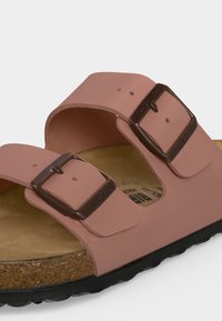 Κοντινή λήψη ενός ροζ σανδάλι Birkenstock με δύο ρυθμιζόμενους ιμάντες και αγκράφες σε φελλό σόλα και μαύρο καουτσούκ πάτο.