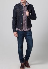 Jeansjacka med kopparfärgade detaljer, rutig skjorta, blå jeans och bruna stövlar. Jackan har fickor och kontrastsömmar.