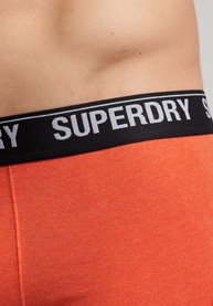 Bóxer de algodón naranja con una cinturilla elástica negra que presenta el logo en blanco "SUPERDRY". Primer plano de la cinturilla y la textura del tejido.