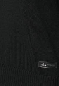 Mustmust rinnaga ja varrukaotstega must kudum, millel on küljes väike must silt valgete tähtedega "A|X ARMANI EXCHANGE".