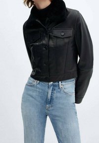 Chaqueta de cuero negra cortada con un suave cuello de piel negra, que presenta dos bolsillos en el pecho y cierre de botones; combinada con unos jeans de color azul claro.