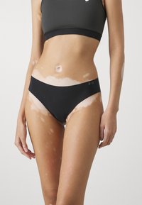 Bas de bikini noir au design épuré, fabriqué en matériau doux. Doté d'une taille basse, de bords sans couture et de détails logo subtils.