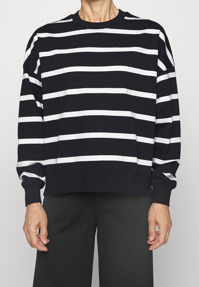 Sudadera negra con rayas horizontales blancas, cuello redondo y mangas largas. Tejido suave con puños y dobladillo acanalados.