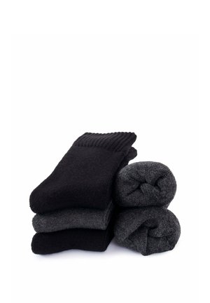 Stack of three folded black and gray socks on the left with two rolled pairs of dark gray socks on the right, on a white background.