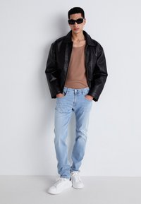 Chaqueta de cuero negra, top de tirantes marrón, vaqueros de mezclilla azul claros y zapatillas blancas. Los accesorios incluyen gafas de sol negras y un diseño minimalista.