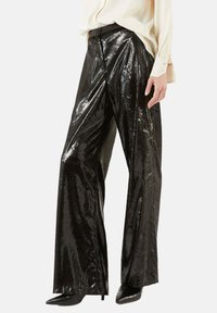 Glänzende schwarze weit geschnittene Hose aus strukturiertem Stoff, mit einem Frontverschluss und einer hohen Taille, kombiniert mit einem hellen Oberteil.