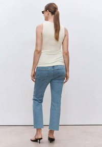 Top sin mangas ajustado color crema combinado con unos jeans rectos de mezclilla azul claro. Los jeans tienen un dobladillo sin acabar y un detalle minimalista en los bolsillos traseros. Sandalias negras de tacón bajo.