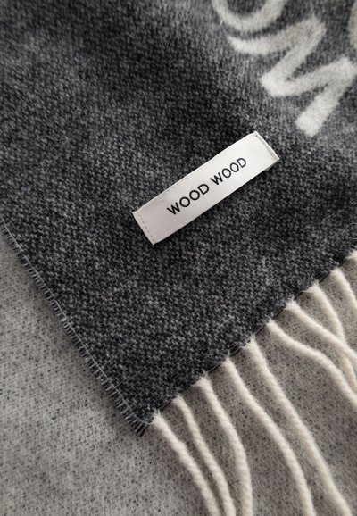 Hallitusvillane sall, millel on tekstureeritud muster, äärtes franja ja valge silt, millel on kirjutatud "WOOD WOOD". Pehme tunne, paks kangas.