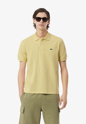 Polo shirt gialla con colletto, maniche corte e logo verde sul petto, abbinata a pantaloni verde olivo.