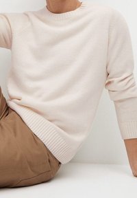 Jasnoróżowy dziergany sweter z okrągłym dekoltem, ściągaczami na mankietach i dole. Tkanina wydaje się miękka i lekko teksturowana.