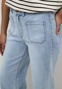 Light blue denim jeans with a straight-leg design, featuring a button closure and subtle stitching details on the pockets.