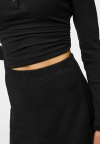 Zwarte geribde longsleeve top met een aansluitend design, gecombineerd met een zwarte, gestructureerde high-waisted rok, die eenvoud en comfort benadrukt.