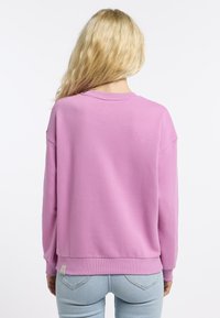 Volné růžové tričko s žebrovaným kulatým výstřihem a manžetovými rukávy, vyrobené z měkkého materiálu. Pohled zezadu neukazuje žádné další vzory nebo ozdoby.