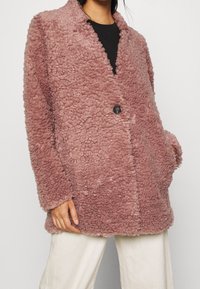 Jakke i imiteret pels i støvet rosa med notch-krave, enkelt knaplukning og sidelommer. Blød tekstur med et blødt udseende.