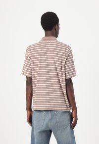 Kortærmet, collaret polo skjorte i lys brun med hvide vandrette striber. Stoffet fremstår blødt med en afslappet pasform og et minimalistisk design.