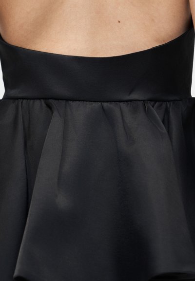 Vue arrière d'une personne portant une robe noire sans bretelles avec une ceinture en satin ajustée et une jupe en tulle plissée, dévoilant la peau du haut du dos et un grain de beauté.