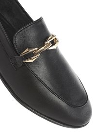 I mocassini in pelle nera presentano una punta affusolata e una prominente accentuazione con catena dorata sul dorso, con cuciture eleganti e una superficie liscia.
