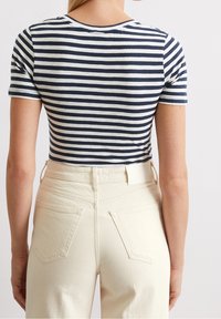 Stribet t-shirt i navy og hvid, kortærmet, rund hals; båret med højtaljede cremefarvede jeans med baglommer.