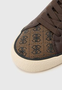 Ruskea lenkkikenkä, jossa on teksturoitu ruskea kangaspäällinen mustalla kuviolla, ruskeat nahkaiset yksityiskohdat ja beige kumipohja.