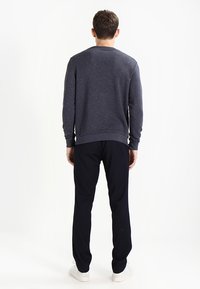 Szara bluza z prążkowanymi mankietami i dołem, zestawiona z czarnymi spodniami. Całość dopełniają białe trampki, widok od tyłu.