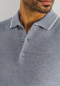 Grijs textuur polo-shirt met een klassieke kraag, contrasterende witte afwerking en twee knoopsluitingen met een klein gaatje bij de hals.