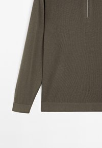 Olivengrøn strikket pullover med lange ærmer, der har en halv lynlås krave og ribbede manchetter og forneden. Glat tekstur med diskret glans.