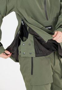 SLOPE® jacka i olivgrön; har vattentåligt tyg, fickor med dragkedja och tryckknappar, samt en kontrasterande svart meshinredning.