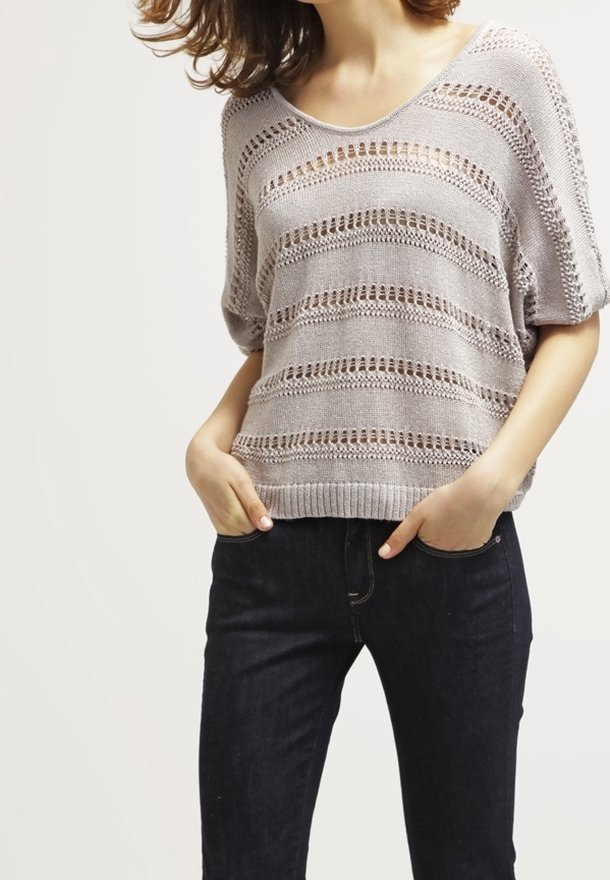 Pull en maille gris clair avec des rayures ouvertes horizontales, un col large et des manches courtes, associé à un jean noir.