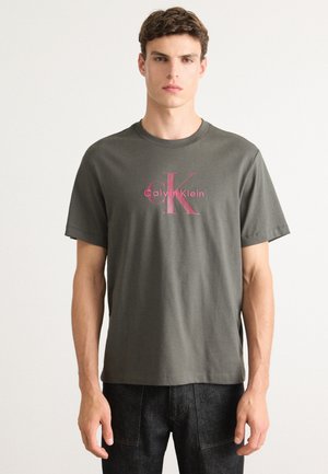 Olivegrünes Baumwoll-T-Shirt mit einem pinken Calvin Klein-Logo und einem Rundhalsausschnitt. Kurzärmlig mit geradem Saum und weicher Textur.