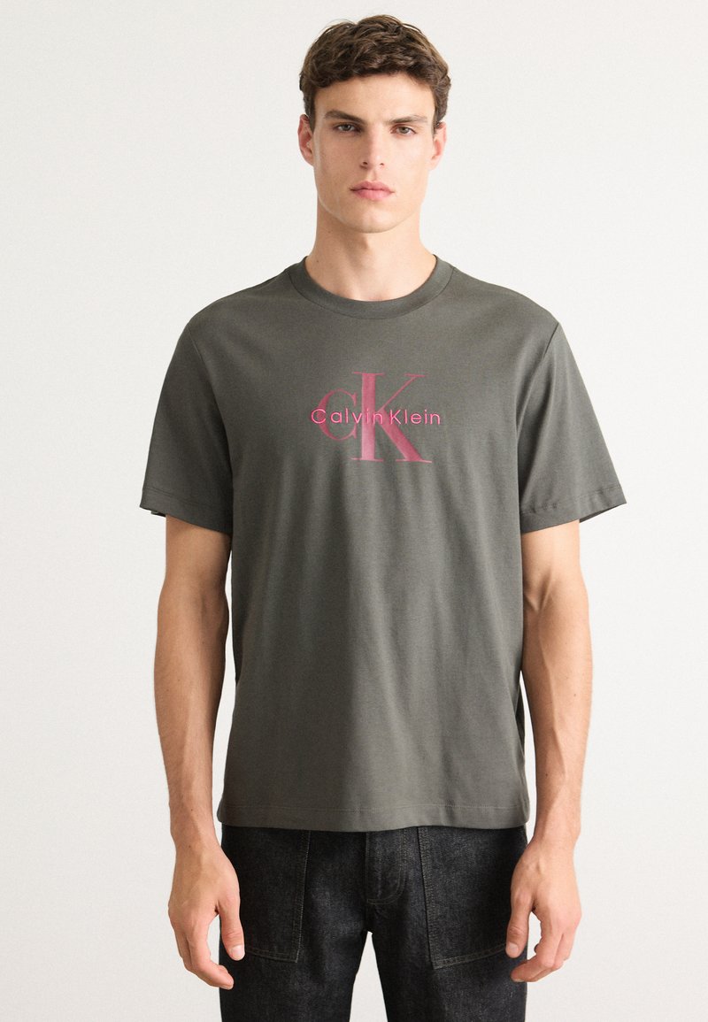 Maslinasta pamučna majica s kratkim rukavima, s ružičastim Calvin Klein logotipom i okruglim izrezom. Ravnog kroja, ugodne teksture.