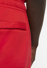 Rode fleece joggers hebben een achterzak, een elastische tailleband en een gladde textuur, met zichtbare stikseldetails.