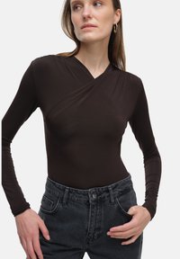 Brązowy bodysuit z długim rękawem o fasonie kopertowym i gładkiej teksturze, zestawiony z ciemnoszarymi, wysokogatunkowymi dżinsami.