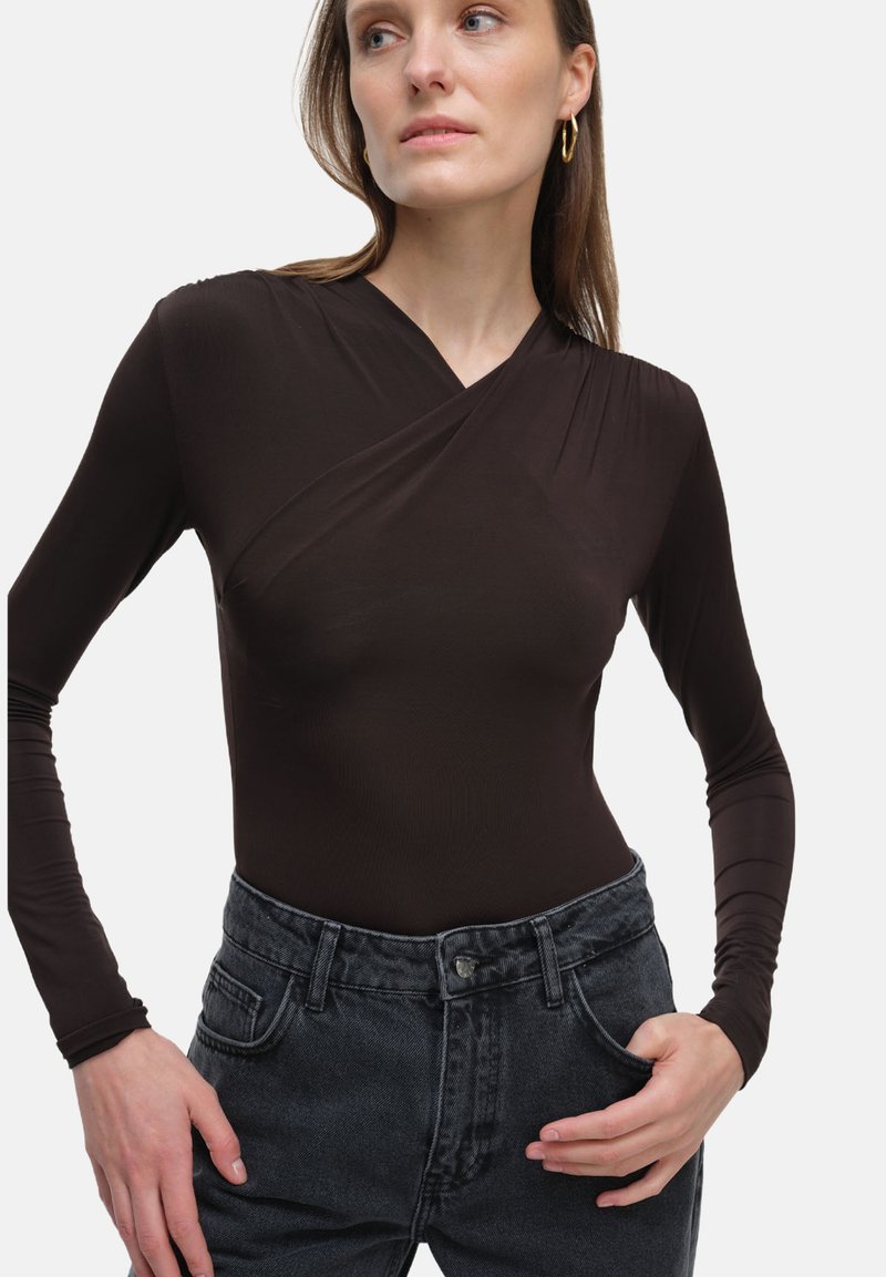 Brązowy bodysuit z długim rękawem o fasonie kopertowym i gładkiej teksturze, zestawiony z ciemnoszarymi, wysokogatunkowymi dżinsami.