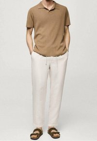 Hnědá polo košile s krátkým rukávem, lehké krémové kalhoty ze lněné směsi se zúženými nohavicemi a hnědé sandály s nastavitelnými popruhy.