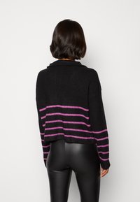 Schwarzer, verkürzter Pullover mit lila horizontalen Streifen, der einen Schal-Kragen und eine lockere Passform aufweist. Strukturiertes Strickmaterial, lange Ärmel.