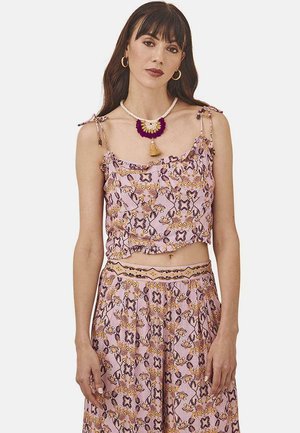 Top corto floral rosa con bordes rizados, patrones intrincados en negro y amarillo. La modelo lleva una falda de talle alto a juego y un collar colorido.