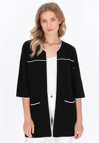 Schwarze Strickjacke mit halben Ärmeln, weißen Besätzen, zweivorderen Taschen und lockerer Passform. Hergestellt aus weichem Stoff und verfügt über ein sauberes Design.