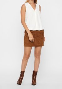 Haut blanc sans manches avec un décolleté en V et une mini-jupe en daim marron. Bottes à talons marron complètent la tenue. Tissu lisse et design simple.