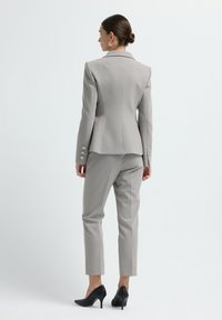Blazer ajusté gris avec un design cintré et des épaulettes, associé à un pantalon taille haute assorti. Des escarpins noirs texturés complètent le look.