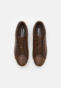 Baskets en cuir marron avec une texture lisse, dotées de bouts ronds, de lacets ton sur ton et d'une semelle en caoutchouc blanche. Logo embossé sur la languette.