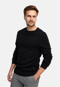 Czarny dziany sweter z ukośnym prążkowanym wzorem, okrągłym dekoltem i długimi rękawami. Posiada dopasowany dół oraz subtelny akcent z logo po bokach.