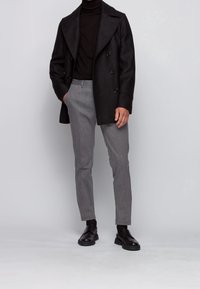 Czarny dwurzędowy płaszcz, dopasowany czarny golf, szare wzorzyste spodnie oraz czarne sznurowane buty. Czyste linie i dopasowany krój.