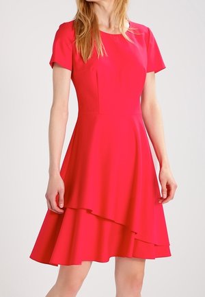 Vrouw draagt een felrode, korte mouwen jurk met een gelaagde, asymmetrische rok en een aangesloten taille.