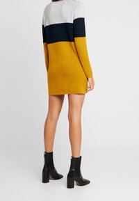 Vestito a maglia color block con colori grigio, blu navy e senape; realizzato in tessuto morbido; orlo a coste; indossato con stivali alla caviglia neri.