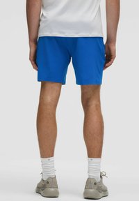 Blaue Sportshorts mit elastischem Bund, glatter Textur und lässigem Schnitt, kombiniert mit weißen Socken und neutral gefärbten Turnschuhen.