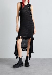 Svart ärmlös klänning med strukturerad stickad design, med sidoklyftor och fransdetaljer. I kombination med svarta ankelskor.