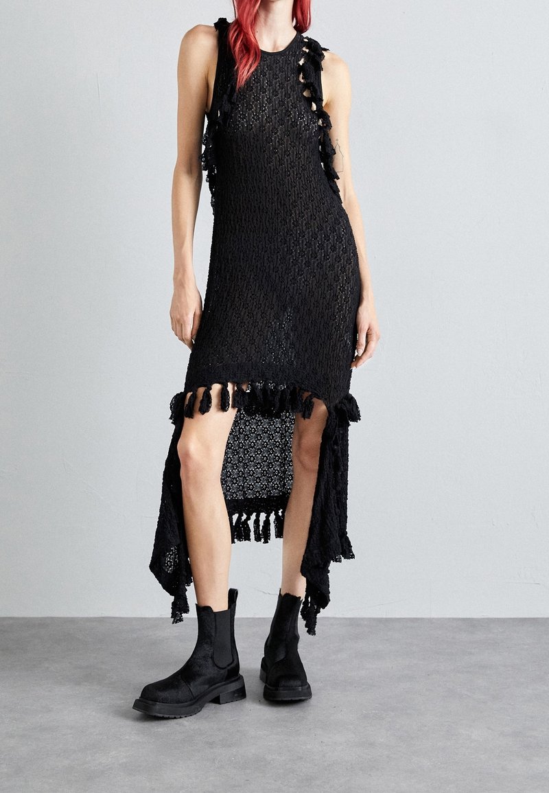 Svart ärmlös klänning med strukturerad stickad design, med sidoklyftor och fransdetaljer. I kombination med svarta ankelskor.